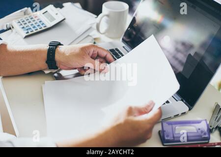 Mani di uomo d'affari che tengono carta bianca con computer portatile e calcolatrice. Contabilità. Foto Stock