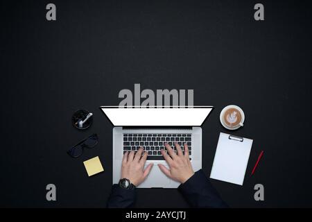 Uomo d'affari mani che lavorano con il laptop . Disposizione piatta e vista dall'alto con materiali di consumo per ufficio e spazio per la copia su sfondo nero Foto Stock