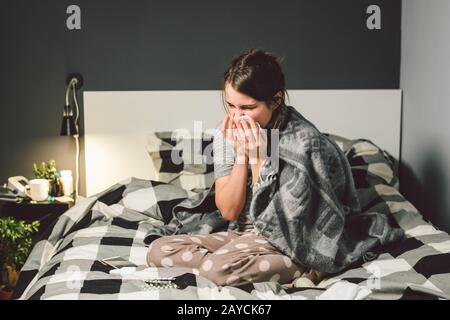 donna malata con naso che cola, seduta a letto, malessere e starnutire la camera da letto. Donna che tiene il tessuto, sintomi di influenza. Healthc Foto Stock