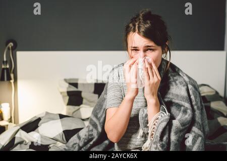 donna malata con naso che cola, seduta a letto, malessere e starnutire la camera da letto. Donna che tiene il tessuto, sintomi di influenza. Healthc Foto Stock