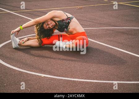 Donna Athlete Allunga Le Gambe Sullo Stadio. Runner Femminile Che Si Allunga Prima Dell'Allenamento. Ritratto di lifestyle della ragazza atletica che fa la guerra Foto Stock