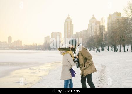 Tema amore e data sulla natura. Giovane coppia eterosessuale caucasica ragazzo e ragazza bacio abbracciare sciarpa calda in inverno vicino a un congelato Foto Stock