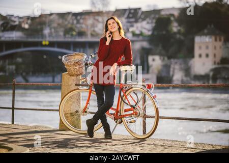 Una giovane viaggiatore femminile che gode si trova accanto a una bicicletta vicino a un fiume nella città di Basilea. Viaggiare in Svizzera. Giovane cau Foto Stock