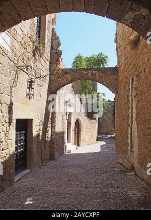 una tranquilla strada medievale acciottolata nella città di rodi con vecchi edifici e archi tra edifici in pietra Foto Stock