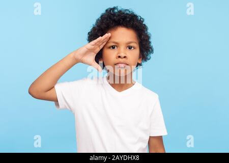 Sì, Signore! Ritratto di bambino serio con capelli ricci che dà il saluto come soldato, ascoltando il comando con espressione responsabile, obbedito a paren Foto Stock