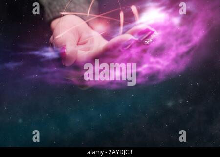 Mano umana che tiene atomo su un palmo. Polvere nebulosa in spazio infinito. Supporti misti. Foto Stock