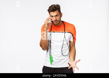 Fastidioso e disturbato sportivo irritato sentirsi arrabbiato qualcuno chiamato durante l'allenamento, rispondere alla chiamata, tenere lo smartphone vicino all'orecchio disple Foto Stock