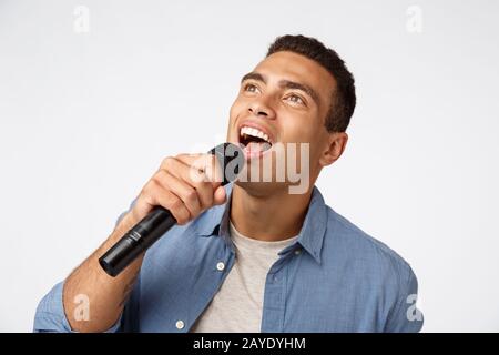Giovane carefree e dal buon aspetto che si diverte durante la festa di natale, cantando la canzone preferita, tenere il microfono piegarsi come la lettura lyr Foto Stock