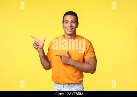 Allegro uomo moderno con braccio tatuato, puntando a sinistra come promuovere il negozio online, invitare ospite unirsi a festa, sorridendo gioiosamente, Recom Foto Stock