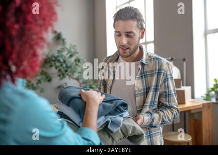 Giovane uomo in una camicia a plaid e una ragazza che si piega vestiti. Foto Stock