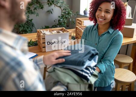 Giovane ragazza e uomo che si piegano vestiti per donazioni. Foto Stock