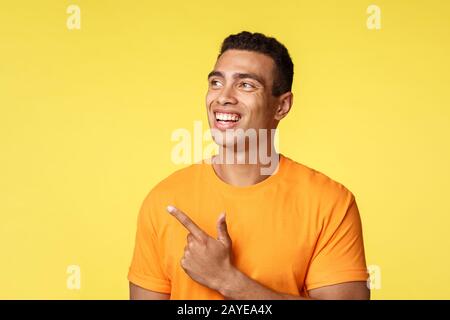 Ispirato, giovane fortunato studente di atletica maschile in t-shirt, guardare interessato e puntando a sinistra, contemplare impressionante albero di natale, e. Foto Stock