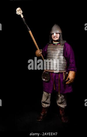 uomo in abito medievale, camicia viola, casco e catena posta tiene una lancia Foto Stock