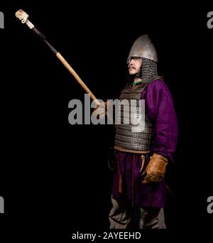 uomo in abito medievale, camicia viola, casco e catena posta tiene una lancia Foto Stock