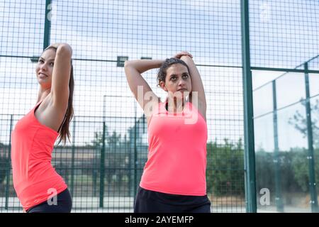 Due ragazze in abbigliamento sportivo che si allungano le braccia su un campo da tennis all'aperto Foto Stock