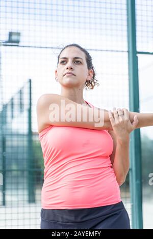 Foto verticale di una ragazza in abbigliamento sportivo che allunga le braccia su un campo da tennis all'aperto Foto Stock
