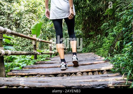 Gambe di una ragazza in tights camminare su un vecchio ponte di legno nel mezzo della foresta nel nord della Thailandia Foto Stock