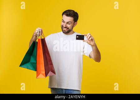 Ritratto di sorridente giovane azienda borse di plastica e carta di credito isolato su sfondo giallo. Foto Stock
