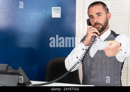 Foto di scorta di un receptionist in uniforme dell'hotel che risponde al telefono mentre dà una scheda della camera Foto Stock