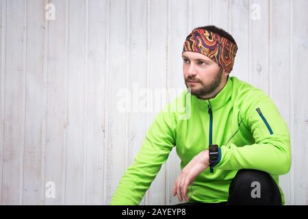 Giovane atleta di aspetto europeo in una giacca verde, guarda, pantaloni neri, si siede. Foto Stock