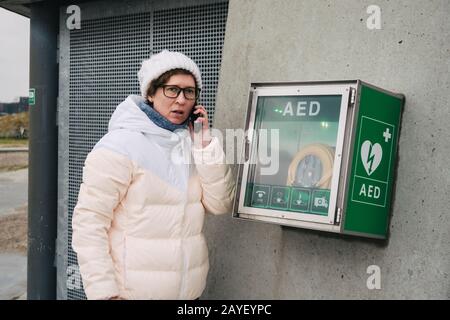 chiamata di emergenza per rianimazione cardiopolmonare medica. La donna caucasica utilizza la chiamata telefonica 911 help. Dispositivo box aed automatico Foto Stock