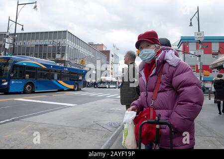 Una donna cinese più anziana fuori dello shopping attende un autobus sulla strada principale a Chinatown, Flushing, Queens, New York City. Foto Stock