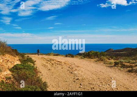 Un giovane che guida una mountain bike su un percorso in bicicletta in Spagna su strada sullo sfondo del Mar Mediterraneo. Vestito Foto Stock