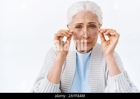 Vecchia ragazza carina senior in pensione casa con capelli pettinati grigi, cant scquinting leggere piccole lettere, piega in avanti, toccando gli occhiali come cercando di concentrarsi su Foto Stock