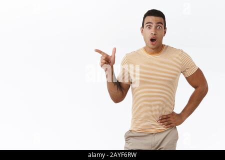 Potete crederlo, guardi. Impressionato, speechless bel maschio giovane maschile, atleta che punta le dita a sinistra, invitando andare sportclub insieme, trovato Foto Stock