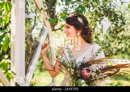 Bella sposa con fiori di bouquet si erge sullo sfondo della foresta. Stile rustico. Bellissima sposa in abiti delicati all'aperto. Clos Foto Stock