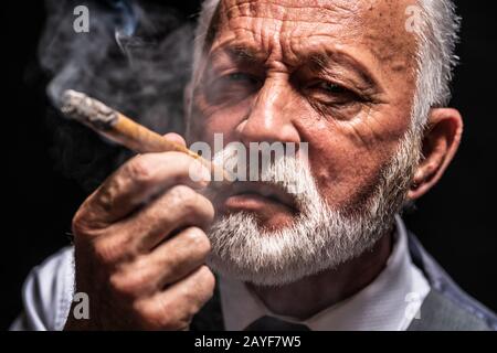 Ritratto di uomo anziano serio che sta smolando sigaro. Foto Stock