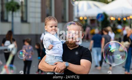 Piazza della Città Vecchia, riga, Lettonia - 16 agosto 2019: Uomo con un bambino sulle sue mani guarda e gioisce alle gigantesche bolle di sapone Foto Stock