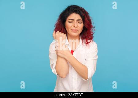 Lesioni alle mani. Lavoratore di ufficio con capelli rossi fantasia in camicia bianca in piedi con grimace di dolore, tenendo il polso dolente, la sindrome del tunnel carpale sofferente. IND Foto Stock