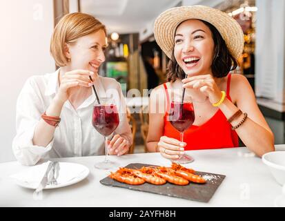 Due amici allegri della ragazza che bevono vino e pranzano al ristorante di pesce Foto Stock