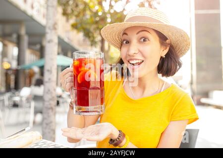 Giovane donna asiatica che beve sangria, tradizionale spagnolo tipo di vino da frutta in un caffè all'aperto Foto Stock