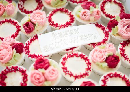 Bella tazza di torte fiori da crema di burro, in colore rosso e rosa con Testo Happy Anniversary su fondente. Foto Stock