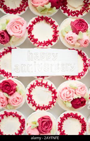 Bella tazza di torte fiori da crema di burro, in colore rosso e rosa con Testo Happy Anniversary su fondente. Foto Stock