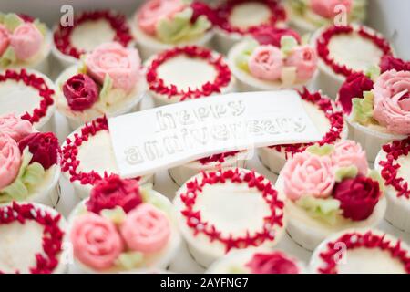 Bella tazza di torte fiori da crema di burro, in colore rosso e rosa con Testo Happy Anniversary su fondente. Foto Stock