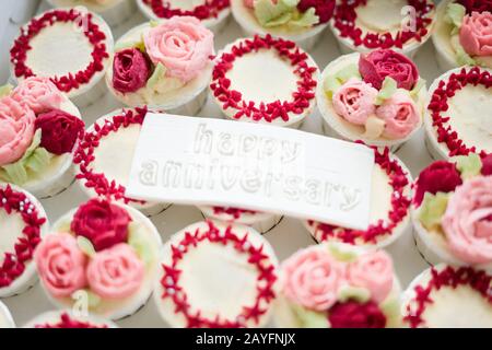 Bella tazza di torte fiori da crema di burro, in colore rosso e rosa con Testo Happy Anniversary su fondente. Foto Stock