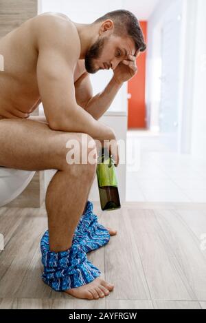 Uomo di ritrovo con una bottiglia di vino seduta sul gabinetto Foto Stock