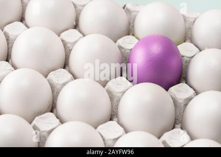 Uovo rosso viola di Pasqua tra molti altri bianchi identici. Il team leader o un loner., simbolo di individualità. Concetto. Foto Stock