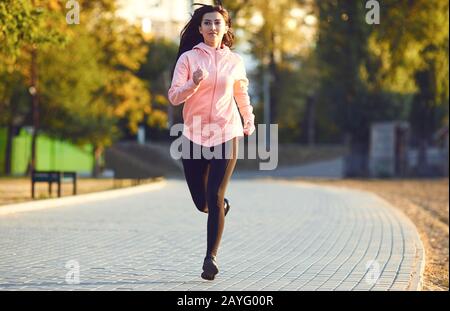 Una ragazza in abbigliamento sportivo corre sulla strada nel parco autunnale. Foto Stock