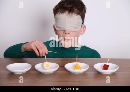 Un ragazzo dai capelli scuri di 8yrs vecchia prende parte a una prova del gusto ciecfold, assaggiando i pezzi di pesca della frutta ciechi Foto Stock