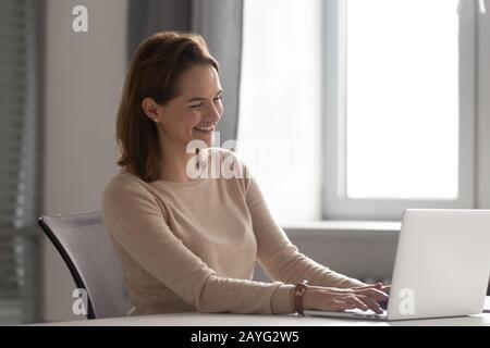 Felice millennial donna sorridente lavorando sul laptop sul posto di lavoro Foto Stock