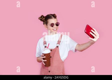 elegante e alla moda, bella ragazza con t-shirt bianca e occhiali da sole, mentre fa selfie foto sul suo smartphone Foto Stock