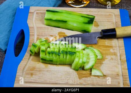 Primo piano di cetrioli crudi freschi e verdi tagliati a fette su tagliere di legno con coltello da cucina giapponese Foto Stock