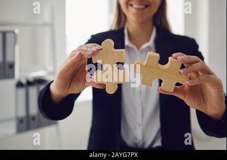 Mani senza volto di una donna d'affari con puzzle in legno in mani in ufficio. Foto Stock