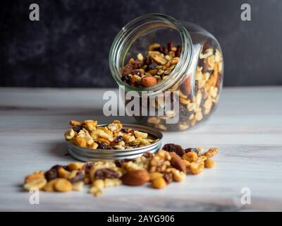 Vaso di vetro riempito con noci sane, semi e uva passa che spargendo fuori, il grasso perfetto di salute e buon carboidrato per fornire nutrizione! Foto Stock