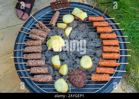 barbecue grill kebab hamburger patate e formaggio di cottura su carbone caldo nel cortile in inghilterra uk Foto Stock