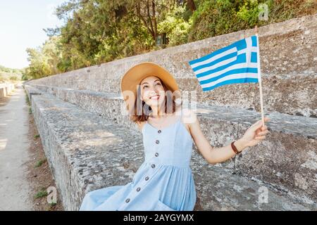 Ragazza asiatica turistica che viaggia nelle rovine di un'antica Acropoli o l'anfiteatro con una bandiera greca. Concetto attivo di giovani viaggiatori e studenti Foto Stock